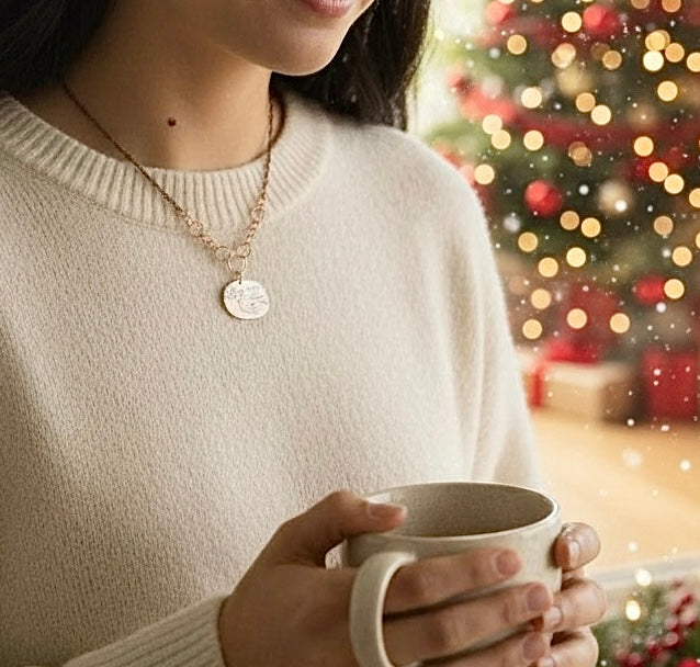 Person wearing a necklace and holding a mug with a Christmas tree in the background