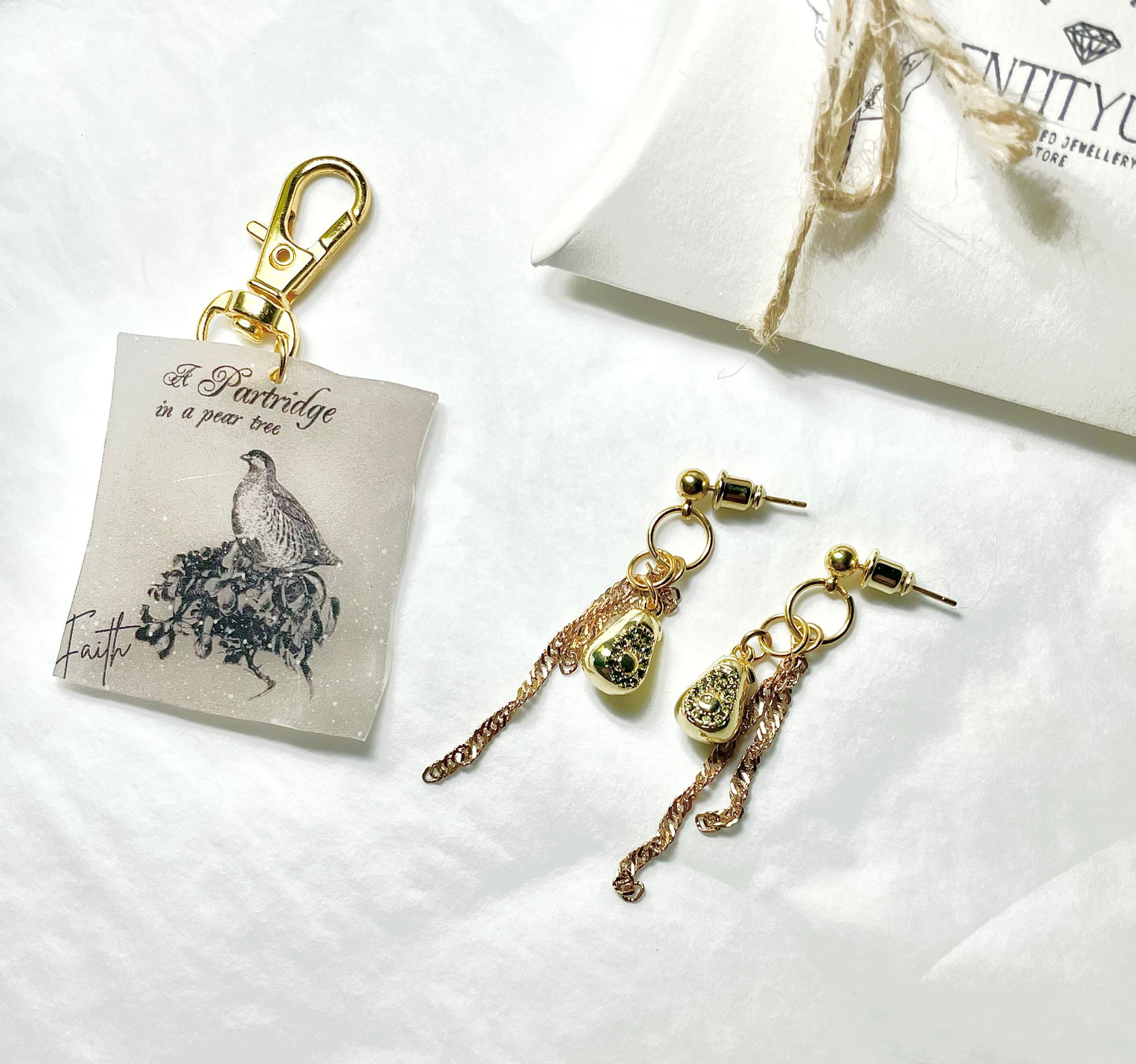 Gold earrings with pear shaped pendants and chain details on a white surface, with a branded jewellery pouch in the background.