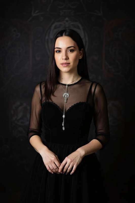 Woman in a black dress with sheer sleeves wearing a silver necklace with moon pendant,  Opalite crystal, and feather and moon charms, against a dark background.