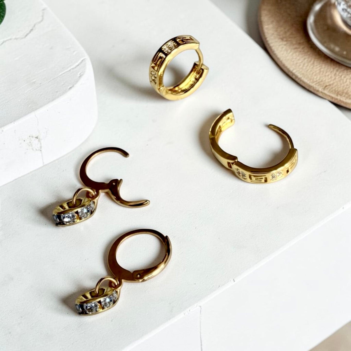 Two pairs of gold hoop earrings: one huggie style, and one dangle with charms, both featuring cubic zirconia.