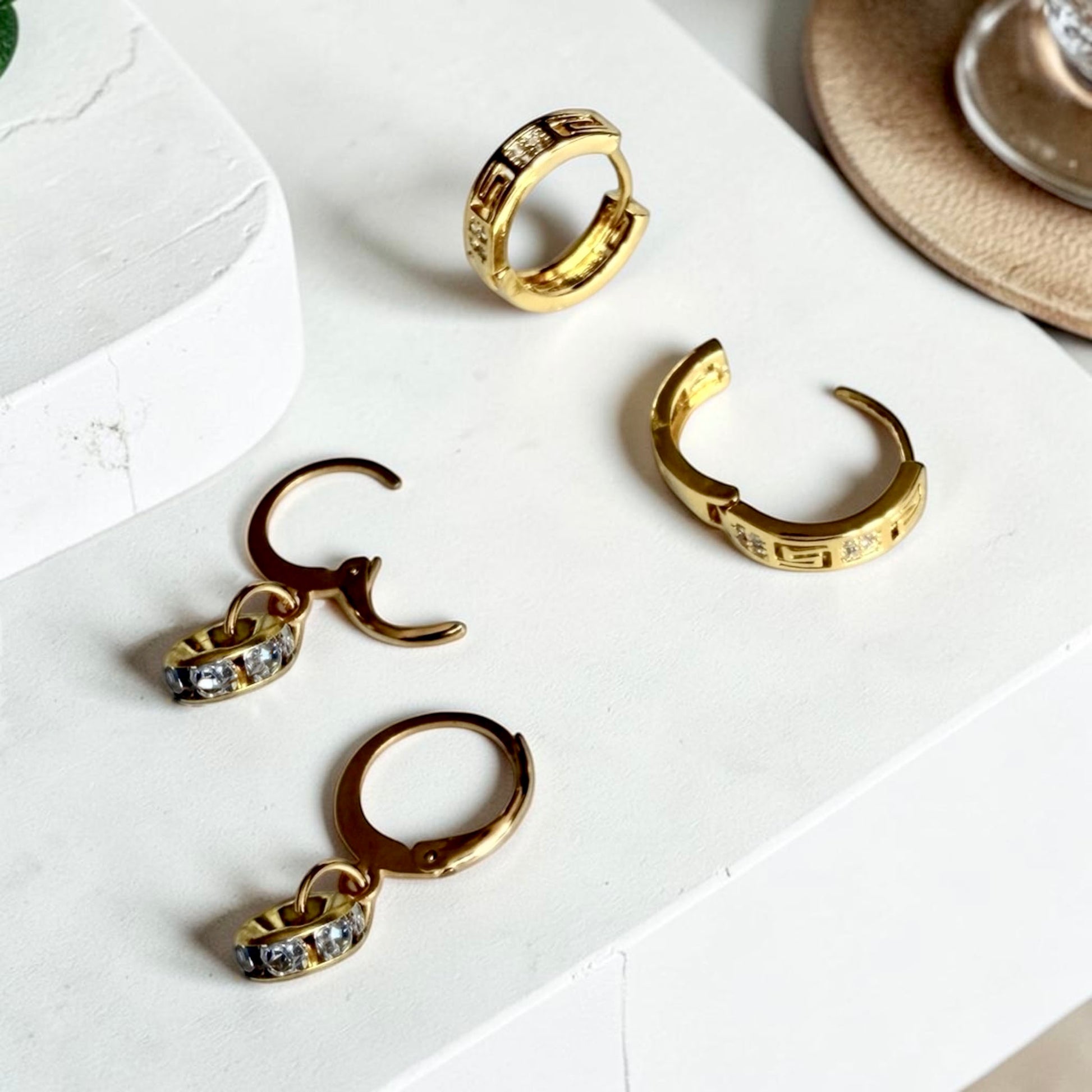 Two pairs of gold hoop earrings: one huggie style, and one dangle with charms, both featuring cubic zirconia.
