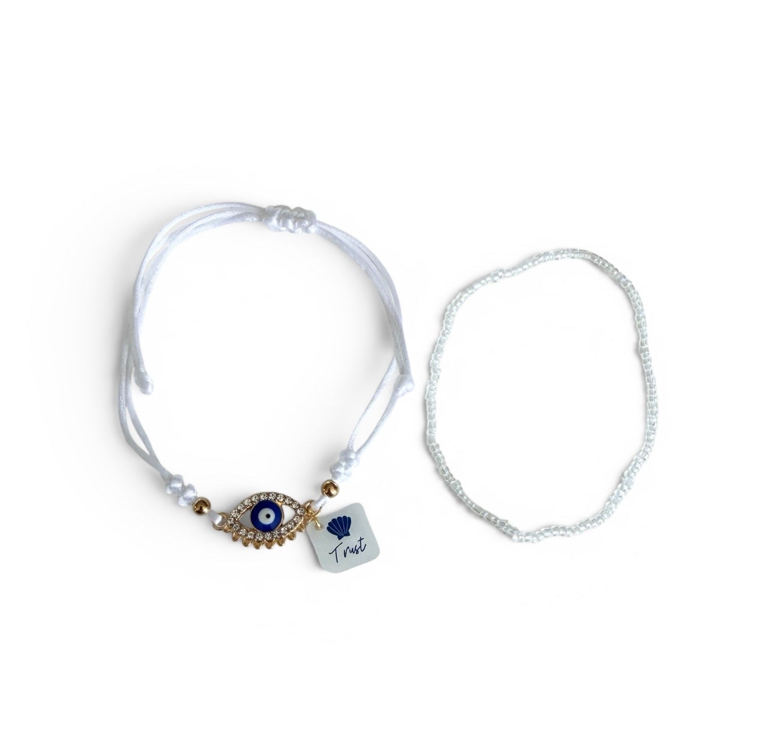 Two delicate bracelets on a plain white background: one white cord bracelet with an evil eye pendant and a small charm marked 'Trust', and one thin white beaded bracelet.