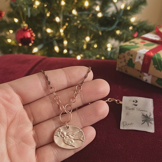 Video of a hand holding a necklace with a Christmas tree in the background
