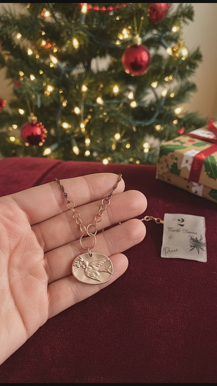 Video of a hand holding a necklace with a Christmas tree in the background